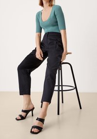 Turkos ribbad bodysuit med vid halsringning, kombinerad med svarta smala byxor och svarta klacksandaler med knutna remmar.