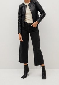 Zwarte leren bomberjack over een crèmewit vest, gecombineerd met hooggetailleerde zwarte cropped jeans met franjes en zwarte enkellaarsjes met hak.