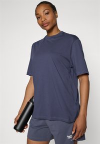 Navy blue cotton T-shirt with a round neckline, short sleeves, and side slits; worn with grey shorts and a black water bottle.