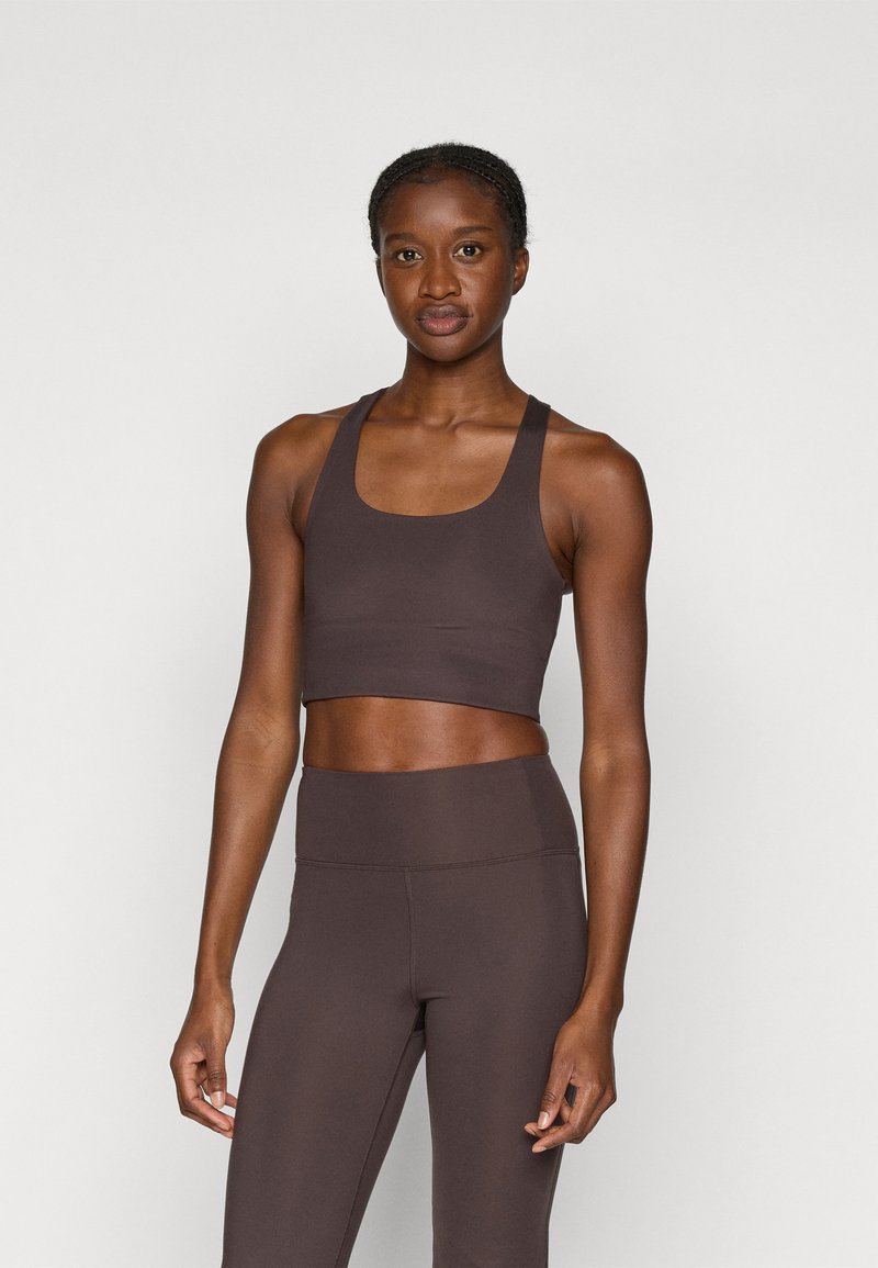 Rudas sportinė crop top su plačiu iškirpimu ir storesnėmis petnešėlėmis, dėvima su aukštos juosmens derančiais džinsais, abu pagaminti iš lygaus audinio.
