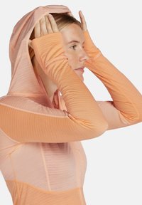 Hoodie léger à manches longues dans des teintes dégradées de pêche, doté de trous pour les pouces, d'une capuche attachée et d'un tissu texturé.