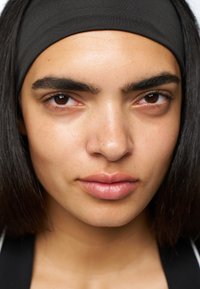 Fascia elastica nera, pelle liscia, carnagione di un marrone chiaro, labbra piene, sopracciglia definite e capelli neri lisci che cadono sulle spalle.