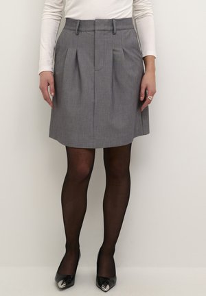 Jupe plissée grise avec une taille structurée, texture du tissu lisse, complétée par des collants noirs transparents et des talons noirs brillants avec des accents métalliques.