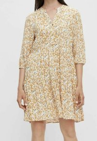 Blumendruckkleid in Creme mit V-Ausschnitt, 3/4-Ärmeln und gerafftem Taillenbereich. Der Stoff ist leicht und hat eine weiche Textur.