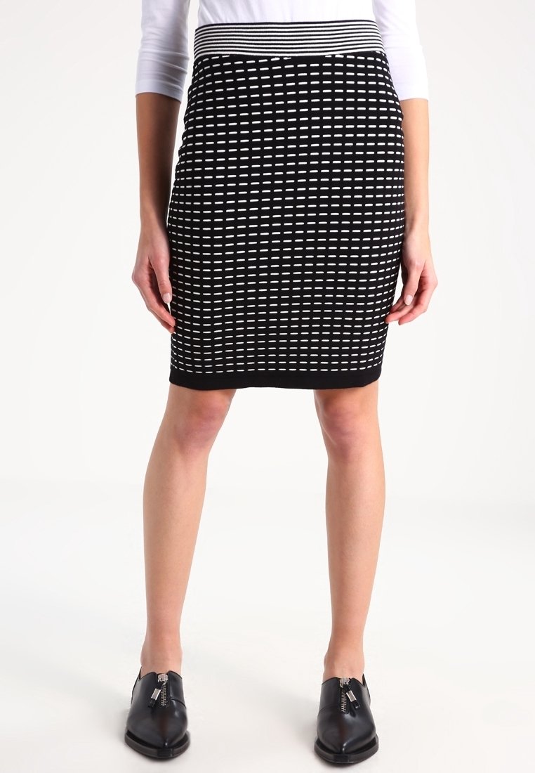 Jupe à motifs noir et blanc longueur genoux portée avec des chaussures noires à fermeture éclair et un haut blanc à manches longues, montrée de la taille aux pieds.