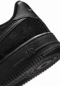 Melnas kedas ar teksturētu zamšādu un ādas augšdaļu, gumijas zoli un iegravētu "AIR" detaļu sānos.