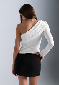 Witte top met één schouder van Textiel en gedrapeerd ontwerp, gecombineerd met een zwarte minirok met een gladde, getailleerde silhouet.