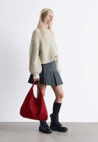 Cremig gerippter gestrickter Pullover, grauer zwiebelförmiger Rock, schwarze schnürbare Kampfstiefel und eine große Handtasche aus rotem Wildleder.