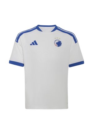 Een jonge jongen staat zelfverzekerd met een voetbal in zijn handen, gekleed in een wit-blauw voetbaltenue met bijpassende sokken en voetbalschoenen tegen een effen achtergrond.
