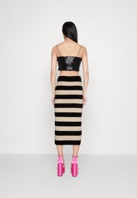 Svart paljettkort topp, beige kjol med svarta ränder och rosa högklackade sandaler med ankelremmar. Bakifrån.