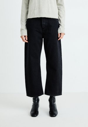 Sorte vide benbukser med høy midje, frontlommer og rett buksdesign. Kombinert med en grå langermet skjorte og svarte støvler.