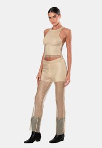 Outfit a due pezzi in rete dorata con top corto e pantaloni trasparenti, caratterizzato da un design aderente e una texture accentuante. Indossato con stivali neri.