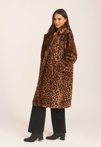 Leopard print faux fur coat with a large collar, front buttons, and side pockets, paired with black wide-leg jeans and block-heeled boots.