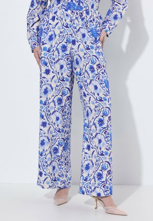 Donna che indossa pantaloni a gamba larga a vita alta e top abbinato con motivo floreale blu, abbinati a tacchi a punta beige in mesh.