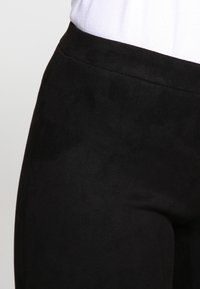Czarne legginsy z zamszu o gładkiej fakturze i dopasowanym kroju, z wysokim pasem zapewniającym komfort noszenia.