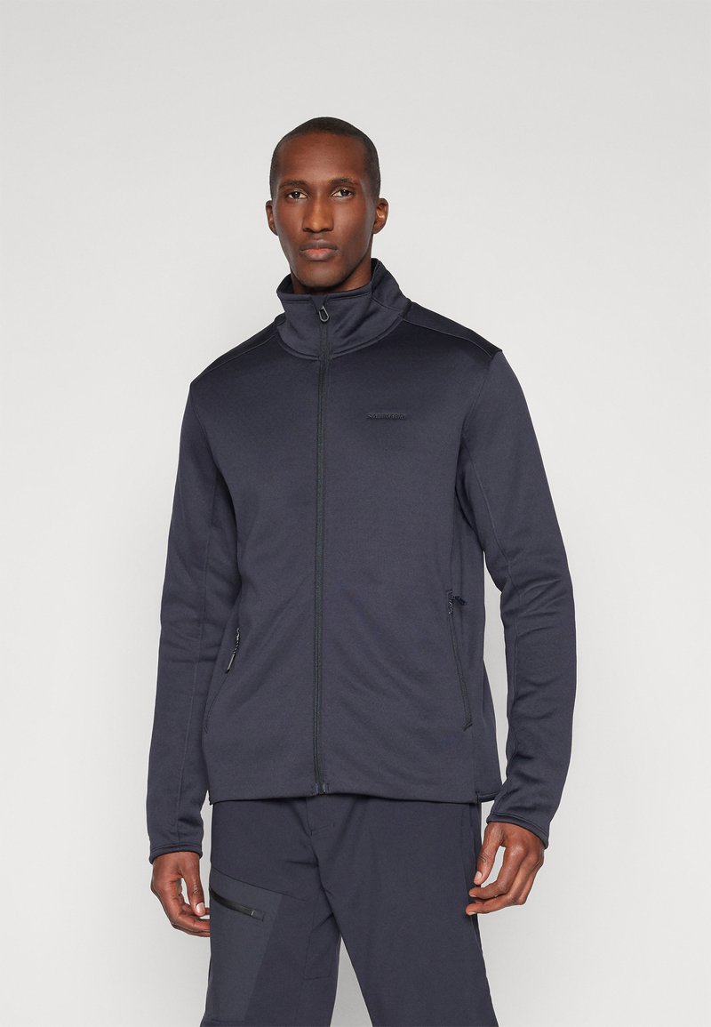 Herre mørkeblå zip-up jakke med høj krave, tætsiddende design og tekstureret stof. Har lynlås-lommer i siderne og kontrasterende syninger.