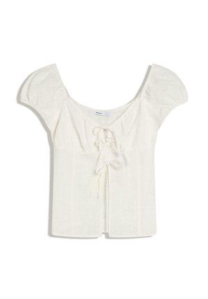 Bílá krátký rukáv košile s hranatým výstřihem a předními detaily s vázáním na jednobarevném pozadí.