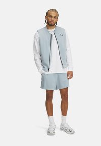 Chaleco de cremalleras azul claro sobre una camiseta de manga larga blanca, combinado con pantalones cortos texturizados azul claro y zapatillas deportivas blancas.
