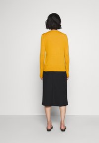 Maglione giallo a maglia con maniche lunghe e scollatura rotonda, abbinato a una gonna midi nera e sandali neri senza chiusura.