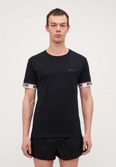 Czarna koszulka z krótkim rękawem i okrągłym dekoltem, z kontrastującą białą i czerwoną elastyczną opaską z logo "Moschino" na rękawach.