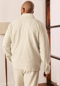 Veste rayée crème avec un large col et des manches longues, associée à un pantalon assorti, présente un tissu texturé et une coupe décontractée.