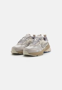Beige athletic shoes with a textured upper, featuring light gray accents and a padded collar, designed for comfort and stability. Sole has blue details.