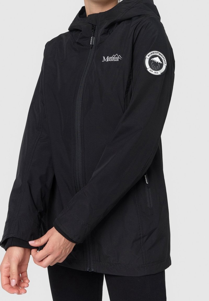 Veste imperméable noire avec capuche, fermeture éclair et poignets élastiques. Présente un logo sur la manche et une texture de tissu lisse.