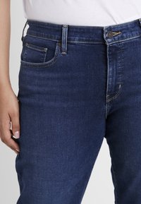 Tummansiniset farkut, joissa on istuva malli, viiden taskun tyyli, nappikiinnitys ja hillityt ompeluyksityiskohdat.