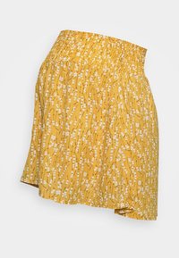 Jupe florale jaune avec une taille smockée. Présente un motif de petites fleurs blanches sur un tissu texturé. Ourlet asymétrique.