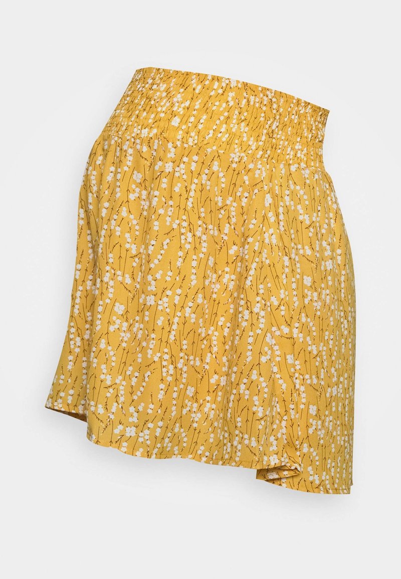 Jupe florale jaune avec une taille smockée. Présente un motif de petites fleurs blanches sur un tissu texturé. Ourlet asymétrique.