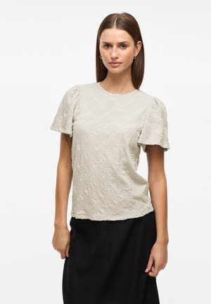 Top a maniche corte di un leggero beige con motivo floreale in rilievo, scollo rotondo e maniche arricciate, abbinato a una gonna nera.