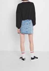 Czarna oversize'owa bluza, dżinsowa spódnica z kwiatowym haftem, białe skarpetki w czerwono-niebieskie paski oraz czarne sneakersy. Swobodny strój.