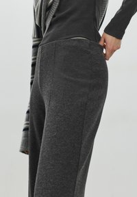 Pantaloni grigi con trama, vita aderente e vestibilità comoda. Presentano cuciture discrete e una finitura liscia del tessuto. Abbinati a una maglia scura.