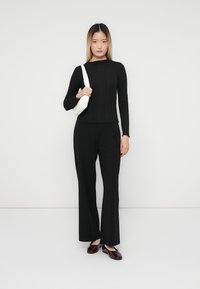 Top negru cu dungi, cu mânecă lungă, asortat cu pantaloni negri, largi. Modelul ține o geantă albă și poartă pantofi burgundii. Outfit simplu, monocrom.
