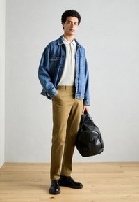 Denimjakke, hvid polo t-shirt, khaki bukser, sorte sko og en sort taske. Moderne, afslappet outfit med en løs pasform og teksturerede materialer.