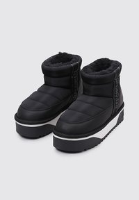 Botas de tobillo negras aisladas con un forro de felpa, parte superior acolchada, entresuela blanca y suela de goma texturizada con un diseño de plataforma baja.