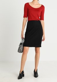 Haut rouge à manches courtes avec un col rond, associé à une jupe crayon noire texturée. Chaussures à talons noires et sac à main à motifs.