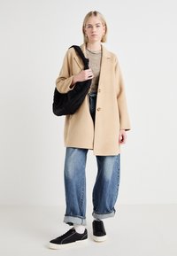 Cappotto in misto lana beige con colletto a rever e due bottoni, abbinato a jeans azzurri larghi e sneakers nere. Borsa nera trapuntata a spalla.
