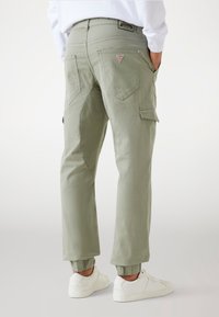Hellgrüne Cargo-Hosen mit elastischen Bündchen, mehreren Taschen und einem Dreiecks-Logo-Patch auf der Rückseite. Hergestellt aus einem strukturierten, strapazierfähigen Stoff.