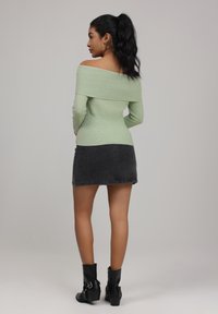 Off-the-shoulder ribbed green top paired with a dark gray denim mini skirt, finished with black ankle boots featuring buckled accents.