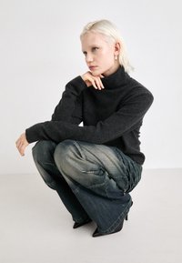 Suéter cinza de gola alta com punhos canelados, combinado com jeans baggy azul claro com detalhes texturizados e sapatos de salto agudo pretos.