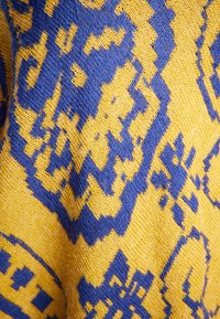 Gebreide trui met een blauw en geel geometrisch patroon, gemaakt van zachte garen, met een gestructureerde afwerking en zichtbare vezels op het oppervlak.