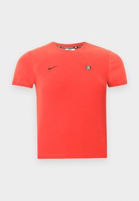 Červené bavlnené tričko s krátkymi rukávmi, na ktorom je čierne logo Nike a malá značková nášivka na hrudi. Jednoduchý okrúhly výstrih.