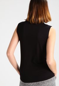 Haut noir sans manches en tissu doux, avec un col rond et une silhouette ajustée. Texture lisse sans motifs ni accents visibles.