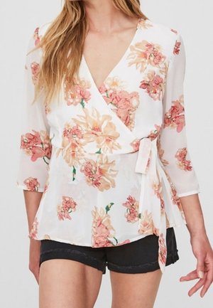 Biała kwiecista bluzka kopertowa z różowymi i beżowymi kwiatami, z rękawami do łokcia i wiązanym w talii, w połączeniu z czarnymi krótkimi spodniami.