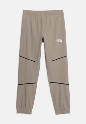 Pantalon de sport marron clair fuselé avec taille et poignets élastiques, rayures diagonales noires, poches latérales et logo The North Face sur la cuisse droite.