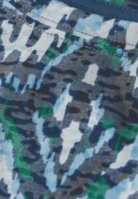 Tessuto a motivi con tonalità astratte di blu, verde e grigio, caratterizzato da una consistenza morbida, utilizzato per un capo di abbigliamento. Cuciture a macchina visibili.