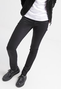 Černé skinny džíny vyrobené z elastického materiálu, s hladkým povrchem a středním pasem. Spárovány s lehkými černými teniskami.