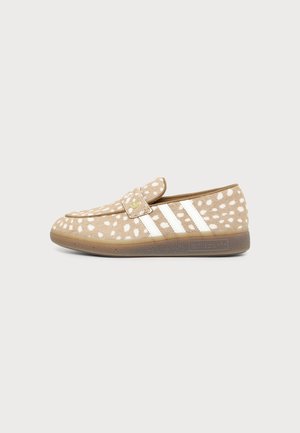 Mocassin beige avec des taches blanches, des bandes blanches Adidas sur le côté et une semelle en caoutchouc avec le logo Adidas.