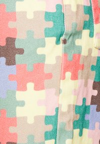 Padrão de peças de puzzle coloridas em um tecido texturizado, apresentando tons de amarelo claro, verde, rosa e marrom em um design repetitivo.